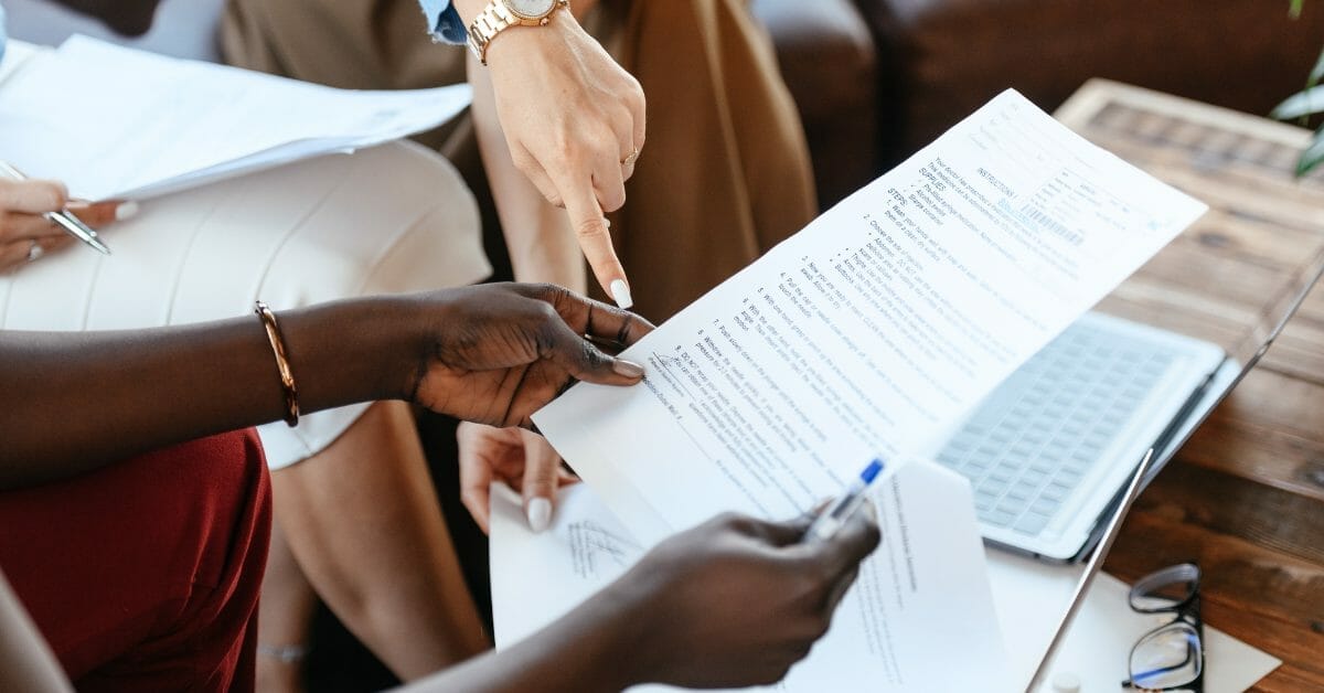 Two professionals from Xseed Lead collaborating on a document titled "5 Tips to Manage Contracts Effectively" at a wooden desk with a laptop in the background.