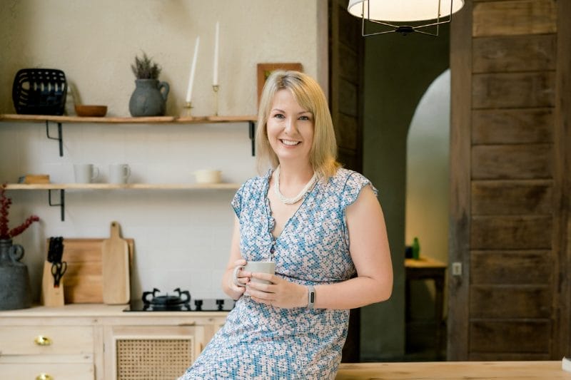 A smiling woman stands confidently in a meeting room with blurred figures in the background, with text overlay about her commitment to empowering women in leadership.