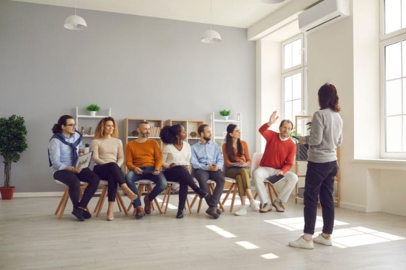 Four professionals are gathered around a table in a well-lit conference room, engaged in a business meeting, with documents, digital tablets, and coffee on the table.