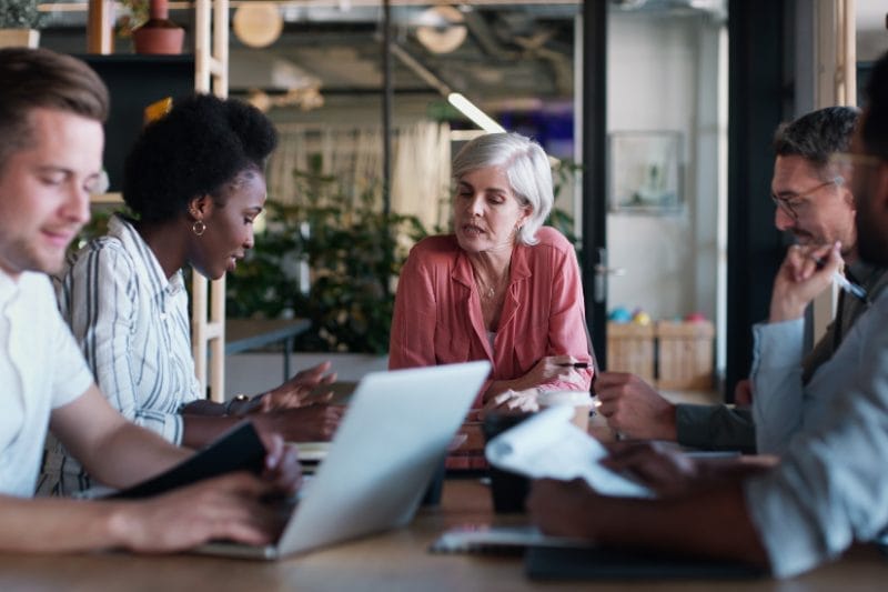 A diverse group of professionals engaged in a discussion around a laptop, representing an Xseed Lead executive coaching session.
