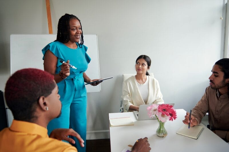 An engaging coaching session led by Xseed Lead, depicted in the blog "Customised Coaching Solutions: Enhancing Professional Growth". The session shows a confident coach in teal speaking to a diverse group of attentive professionals around a table.