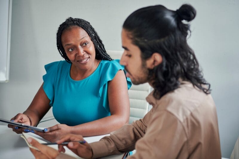Close-up of a coaching session by Xseed Lead, featured in "Customised Coaching Solutions: Enhancing Professional Growth". A coach in teal discusses strategies with a young male professional.