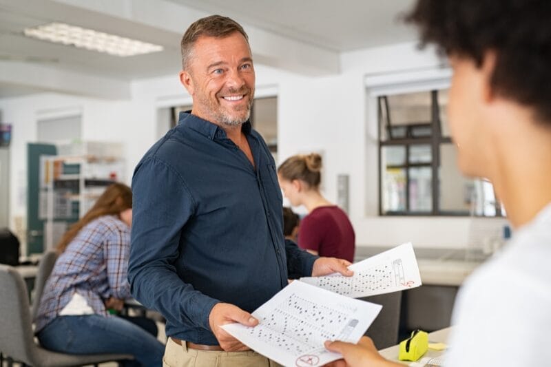 A man handing a document to a colleague in a busy office, discussing promotion feedback.