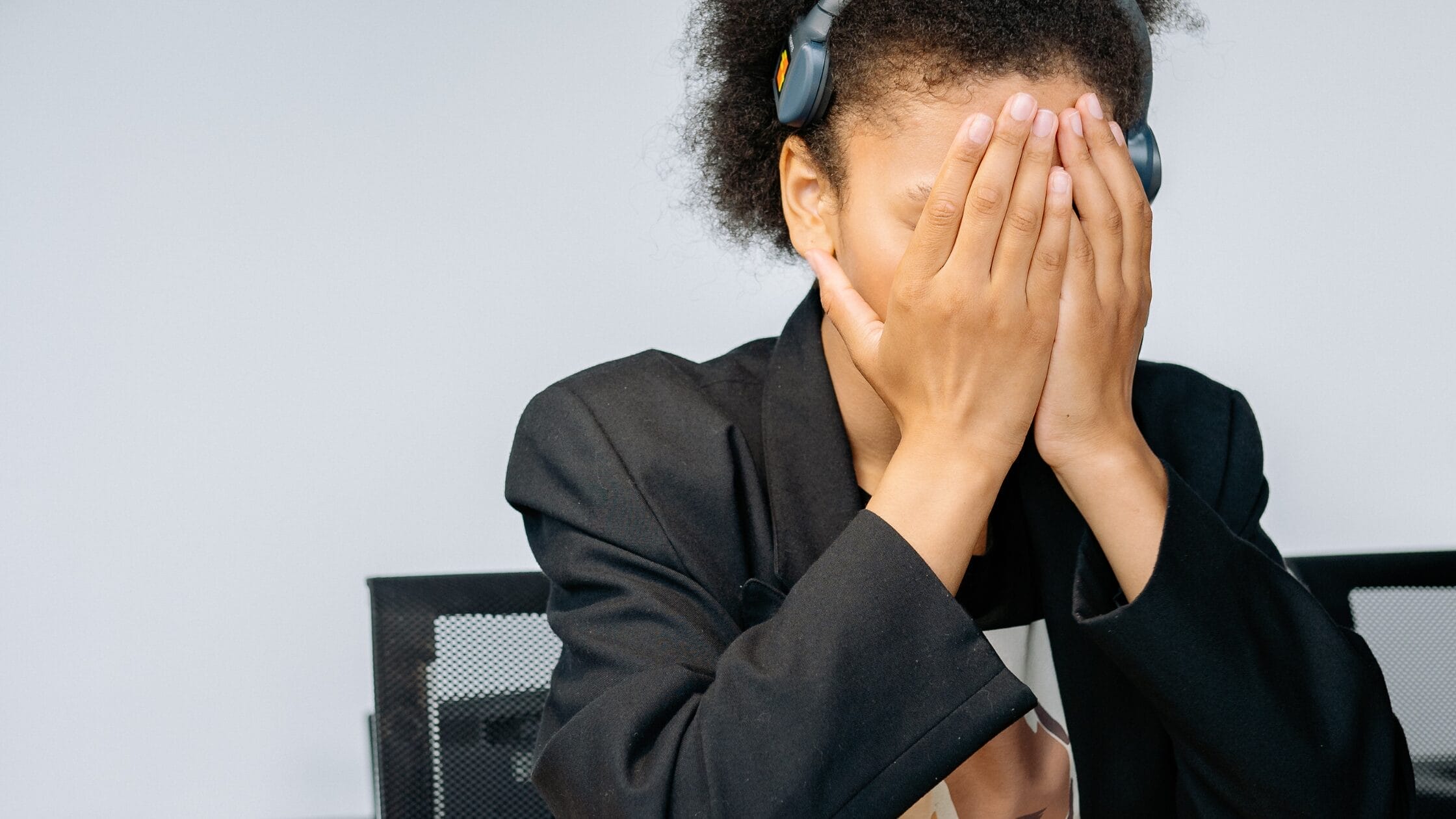 Professional covering her face with her hands while wearing headphones, symbolising workplace pressure and the need for supportive leadership discussed in the blog “Fostering Innovation While Managing Risk” by Xseed Lead.